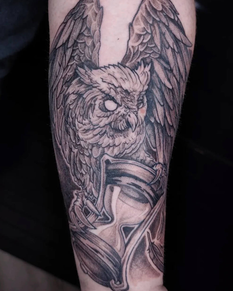 Black and white owl tattoo on a person's arm with a dark background