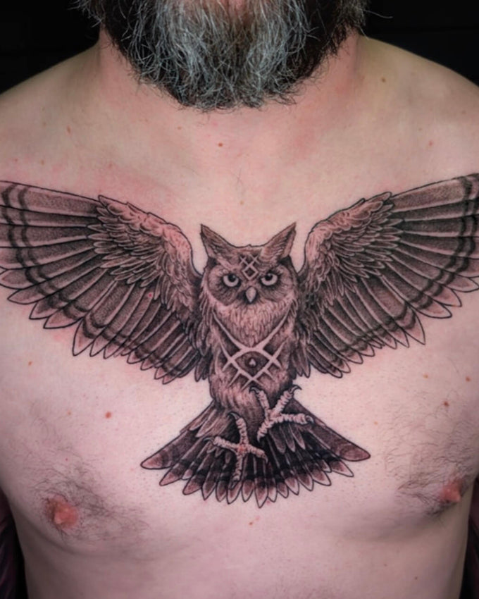 Tattoo of an owl on a person's chest with a dark background