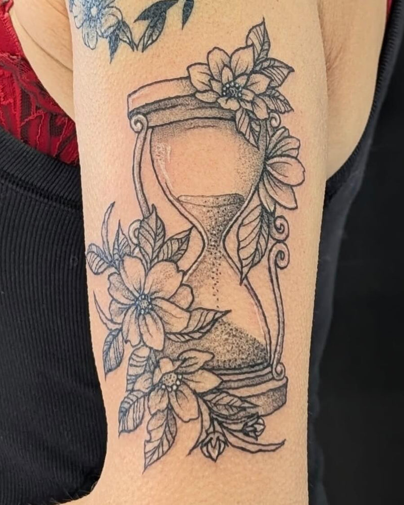 Tattoo of an hourglass with floral elements on a person's arm.