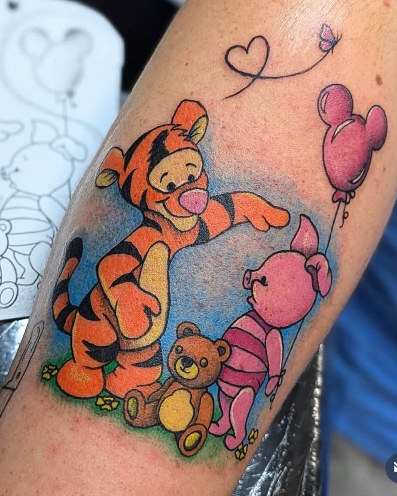 Tattoo of Winnie the Pooh characters on a person's arm with a stencil in the background.