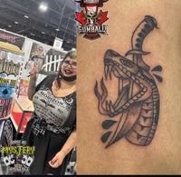 Tattoo artist at convention booth beside a blackwork snake tattoo with bold linework and flame accents on skin