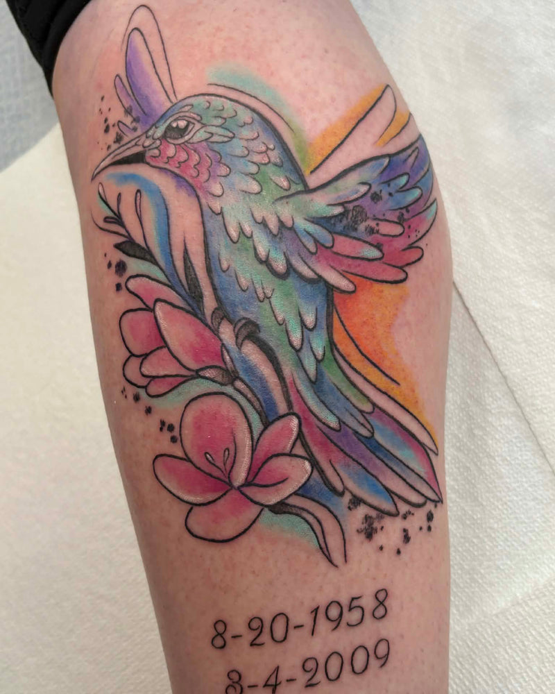 Colorful hummingbird tattoo on a person's arm with dates below.