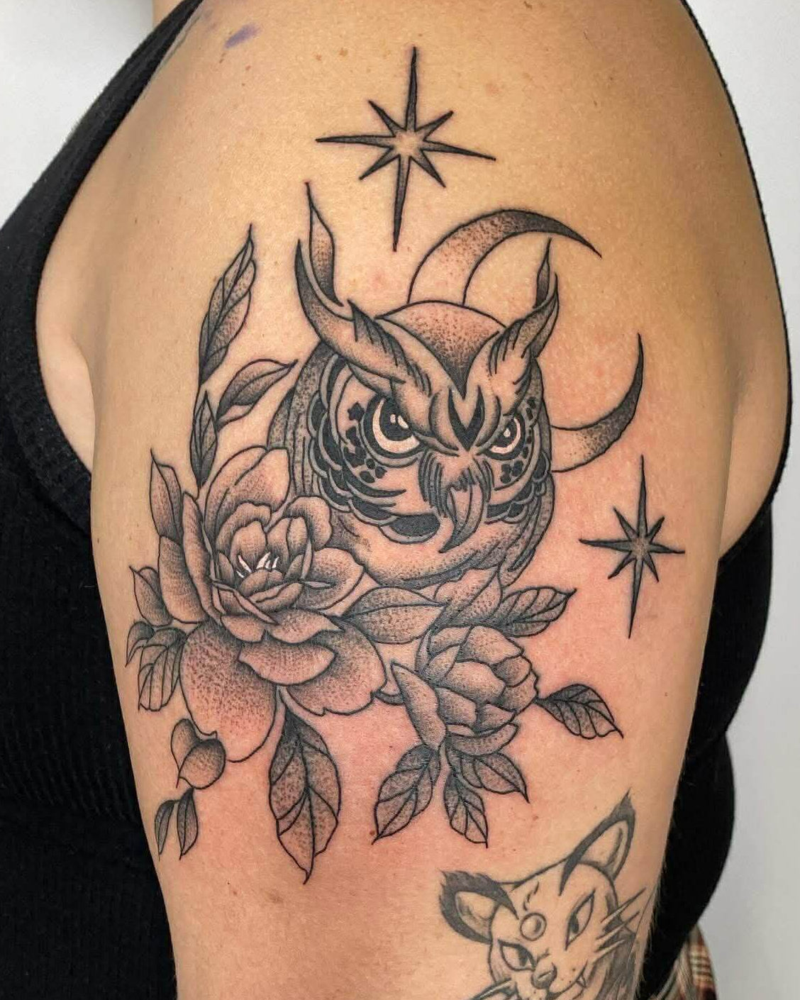 Detailed owl tattoo with flowers and stars on a person's arm.