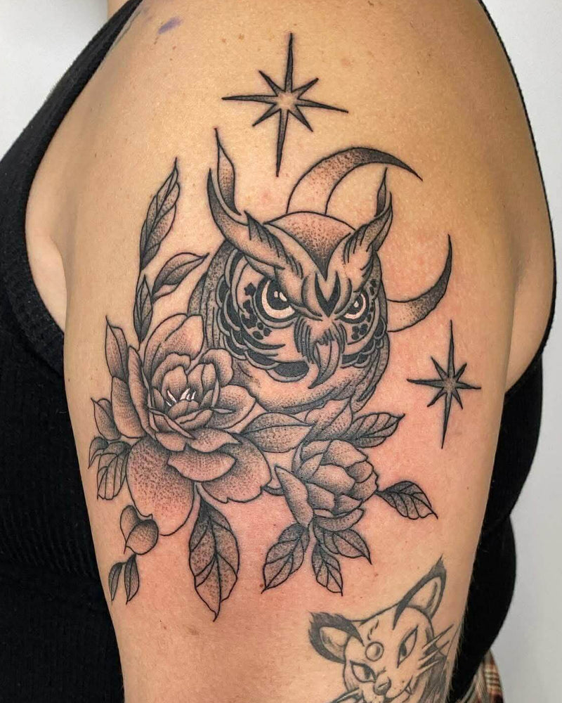 Detailed owl tattoo with flowers and stars on a person's arm.