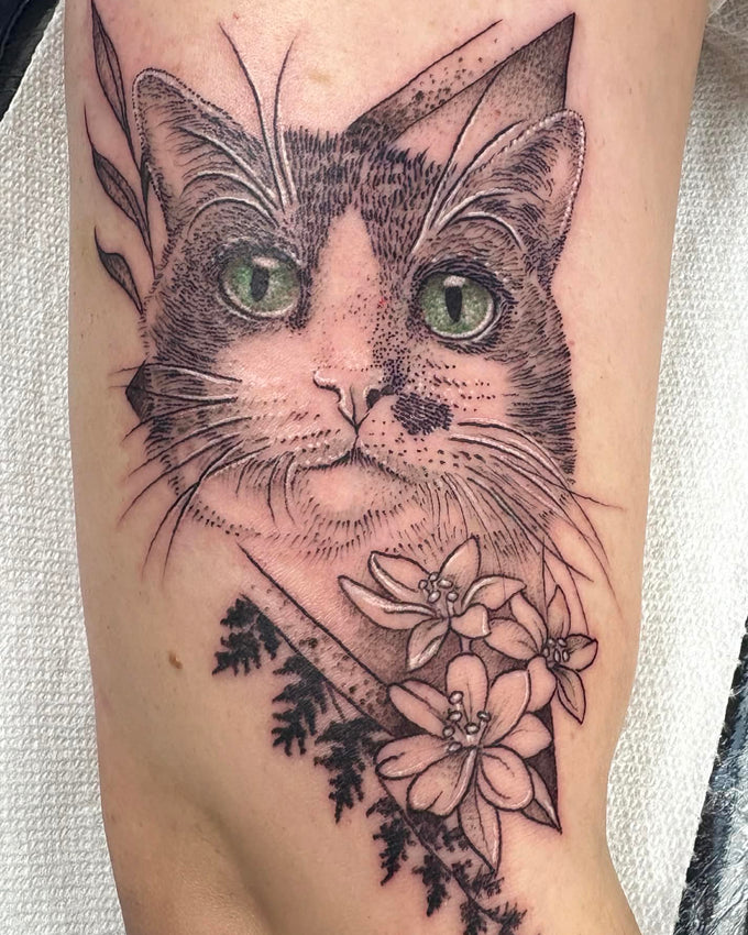 Detailed tattoo of a cat's face with flowers on a person's arm.